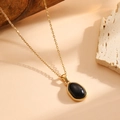 Dettaglio della collana ovale dorata con pietra nera su sfondo di legno e pietra - Collana Nera (A520)