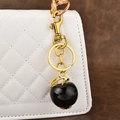 Polished black apple keychain with golden leaf on white quilted bag - Glitter Black