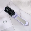 Spazzola pieghevole viola con specchio integrato su sfondo di marmo - Bianco