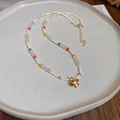 Dettaglio di collana con perline colorate e ciondolo a fungo dorato su vassoio - Bianco/Multicolore