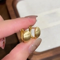 Dettaglio di orecchini huggie dorati con finitura in metallo spazzolato e opaco - Oro