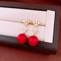Makro-Detail von 18K vergoldeten Ohrhängern mit roter Perle und funkelnden Kristallen - Vierblättrige Blume (Silbernadel)