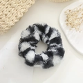 Detail of plush cow print scrunchie with soft faux fur texture on a minimalist desk - Black White Cow Print