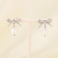 Detail of silver bow earrings with a white pearl drop on a minimalist display stand - Steel Silk Bow (KE115352-KFC)