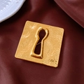 Makroaufnahme einer goldenen quadratischen Brosche mit Hammerschlag-Textur und Schlüsselloch - Gold