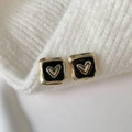 Square black enamel earrings with gold heart detail on white knit background - Black