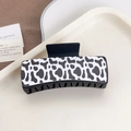 Cow print hair claw clip with black plastic teeth on a neutral display tray - Cow Print