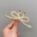 Golden bow hair claw clip with faux pearls and rhinestones shown in hand - Elegant Ribbon Gold