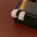 Close-up of silver C-shaped earrings with clear crystals on a black leather box - Silver