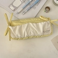 Dettaglio dell'astuccio giallo in tela con fiocco ed etichetta su una scrivania bianca - Giallo/Bianco