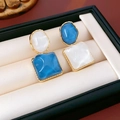 Detailansicht asymmetrischer blau-weißer Resinhart-Ohrringe mit Goldrand in einer Box - Blau