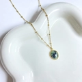 Detailed close-up of a 14K gold plated bohemian necklace with green stone on a white tray - African Pine Stone