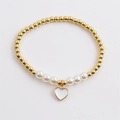 Elastic beaded bracelet featuring gold metal beads, white pearls, and a heart charm - White