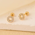 Gros plan de boucles d'oreilles dorées avec zircons blancs sur fond de pierre texturée - Rond Creux / Or Zircon Blanc