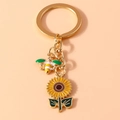 Vista dettagliata dei ciondoli smaltati ape e girasole su un portachiavi dorato - Verde