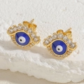 Macro view of gold-plated evil eye stud earrings with blue enamel and clear zircon stones - Royal Blue Evil Eye