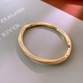Detailed view of a gold-plated twisted bangle with pave-set cubic zirconia on a book - Twisted Style / Gold