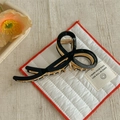 Detail of a black acetate bow hair claw clip with golden metal spring on a soft fabric mat - Solid Black