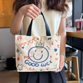 Cream canvas tote bag with blue cartoon crown smile and black handles in casual setting - Happy Face