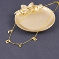 Primer plano detallado de un collar con colgante LOVE dorado en un plato decorativo - Dorado LOVE