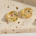 Goldene Blumen-Ohrringe mit bunten Zirkon-Steinen auf einem rustikalen Steinhintergrund - Bunter Zirkon Kreis