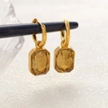 Detail of gold cube earrings with amber rectangle stones on a dark hanging rod - Champagne