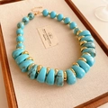 Gros plan d'un collier vintage perlé avec accents dorés et pierres turquoises sur plateau - Bleu