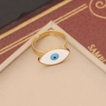 Nahaufnahme des goldenen verstellbaren Evil Eye Rings mit blauer Pupille auf beigem Grund - Ring