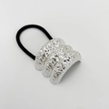 Close-up of silver wrinkled metal texture and black elastic hair tie on a grey background - Sand Silver Triple Design