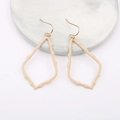 Close-up of beige teardrop earrings with textured hollow design on marble display - Beige