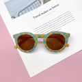Detail van geblokte kinderzonnebril met UV400-glazen op een reismagazine - Blauw-geel ruitje