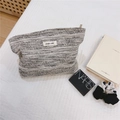 Nahaufnahme der schwarz-weißen Tweed-Kosmetiktasche mit simple wish Label auf Bettwäsche - Vanso Fluss (Schwarz-Weiß Tweed)