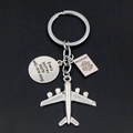 Macro shot of silver airplane keychain with passport charm and inspirational circular tag - Airplane Passport Quote Tag