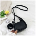 Mini black crossbody bag with embossed girl design and fuzzy pompom charm on white background - Black