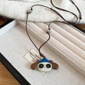 Gros plan du pendentif chien avec chapeau bleu dans un écrin sur tissu blanc doux - Chien avec Chapeau Bleu et Lunettes de Soleil