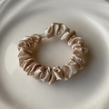 Close-up of a champagne gold satin scrunchie with soft silk texture on a white plate - Beige