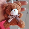 Close-up of a dark brown plush bear keychain featuring a checkered bowtie and soft texture - Brown