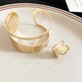 Detailweergave van gouden onregelmatige holle metalen armband en bijpassende ring in een schaal - Armband Ring Set - Goud
