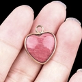 Pink quartz heart pendant with gold plated rim shown held in hand on black background - Rhodochrosite Gold Edging