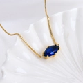 Gold box chain necklace with a blue marquise-shaped gemstone on white shell background - Libra