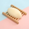 Oval milk white handmade soap bar resting on a slatted wooden soap dish holder - 110g Thai-style Goat Milk Soap