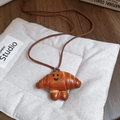 Detail of croissant-shaped pendant with smiley face on brown cord over beige fabric - Leather Croissant Smiley Bread Style