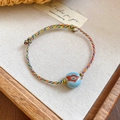 Close-up of handmade bohemian woven cord bracelet with floral pattern ceramic bead detail - Multi-color Cord With Blue Ceramic Flower