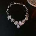 Detail of silver beaded necklace featuring clover, pearl, and camellia charms on dark background - Silver