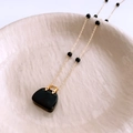 Detail of gold beaded necklace with a unique black handbag pendant on ceramic tray - Gold Necklace-Black Bag Pendant