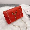 Red leather crossbody bag with golden deer head buckle and chain on white plush rug - Red
