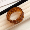Dettaglio di un bracciale in acrilico ambra con sfaccettature geometriche e finitura iridescente - Stile Sfaccettato Geometrico / Caffè Scuro (Consistenza Ambra)