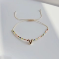 Detail eines böhmischen Perlenarmbands mit goldenem V-Anhänger auf minimalistischem Hintergrund - Buchstabe V