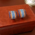 Dettaglio macro di orecchini a lobo curvi con zirconi arcobaleno su astuccio in pelle - Perno per orecchino in argento - Colorato
