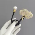 Détail d'un élastique élégant avec perle blanche et pendentifs feuilles dorées en strass - Lys Or